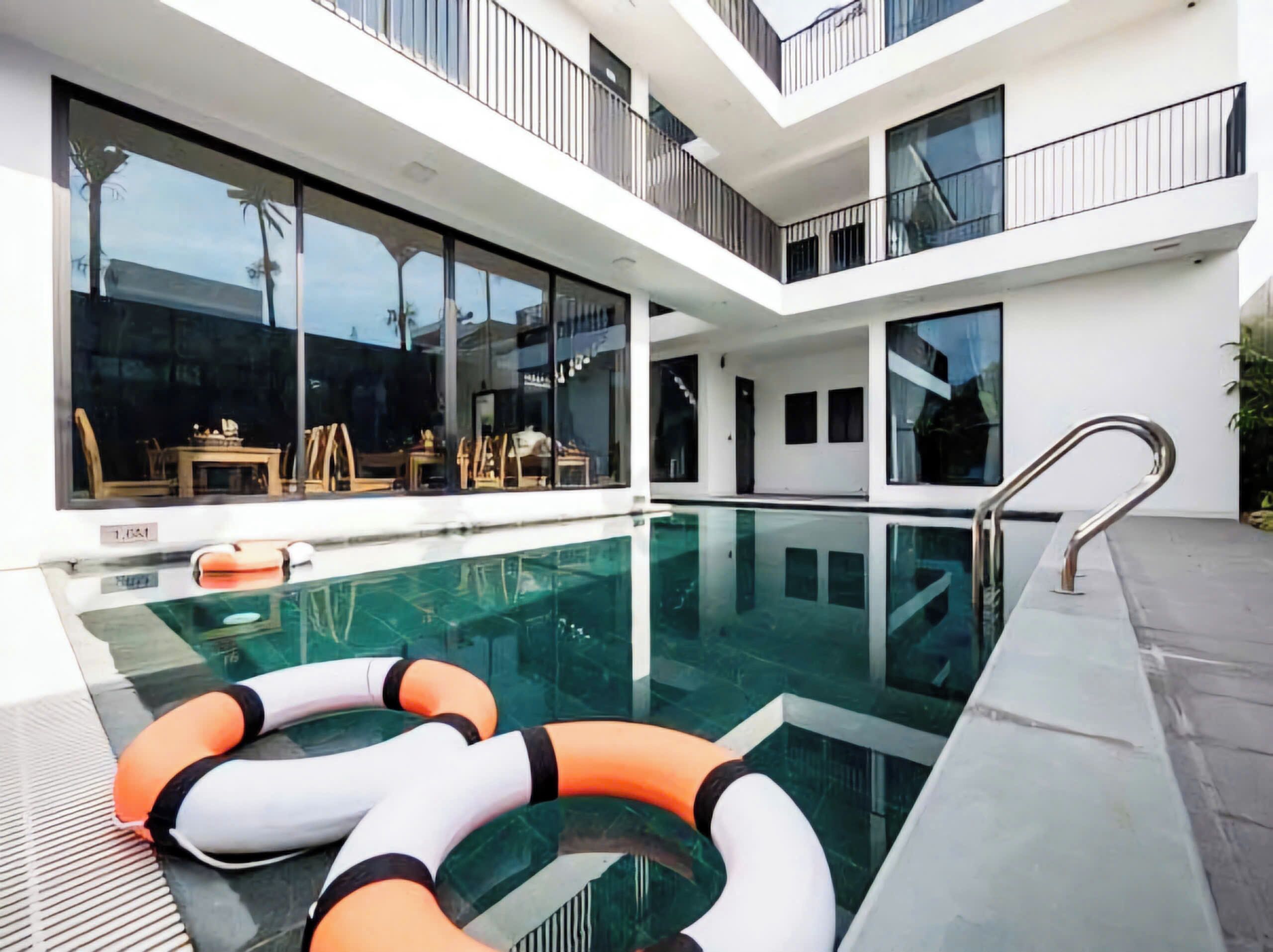 A modern indoor pool with clear glass walls, a floating ring, and a metal handrail.