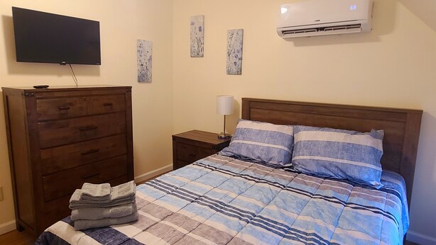 Ein Schlafzimmer mit Bett, Kommode, Fernseher und Klimaanlage.