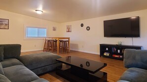 Ein Wohnzimmer mit einer Couch, einem Couchtisch, einem Fernseher und einem Essbereich mit Stühlen und einem Tisch.