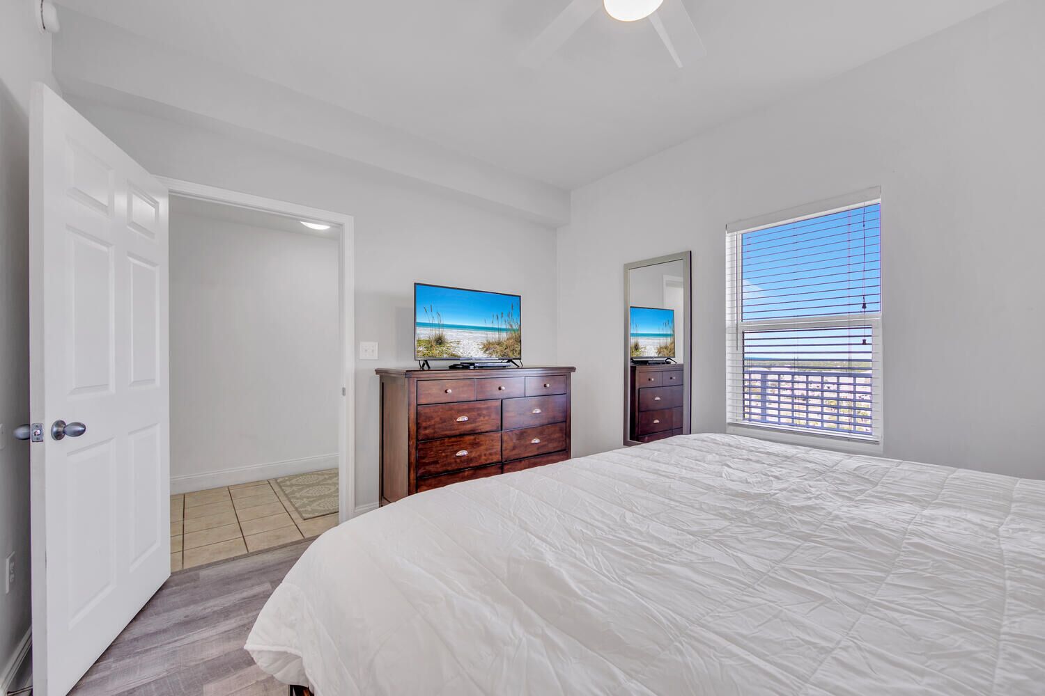 A bedroom with a bed, a dresser, a television, and a window with blinds.