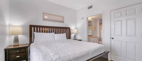 A bedroom with a large bed, two bedside tables with lamps, a ceiling fan, and a white door.