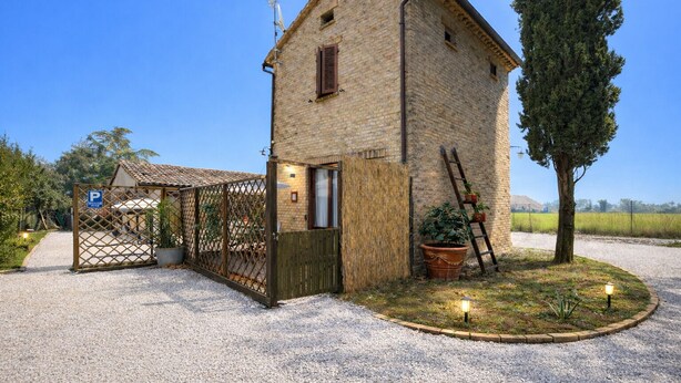 Un bâtiment rustique en pierre, avec une allée de gravier, un portail en bois et un pot de fleurs.