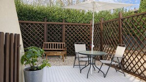 Une terrasse avec un banc en bois, deux chaises, une table et un parasol.