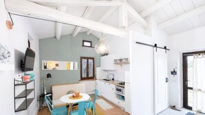 Une cuisine compacte avec des meubles blancs, un coin repas avec des chaises turquoise et une grande fenêtre.