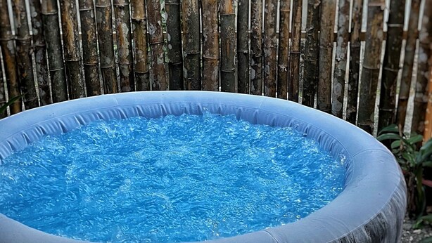 A round hot tub with a wooden exterior, surrounded by a bamboo fence.