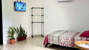 A modern room with a bed, a TV mounted on the wall, an air conditioning unit, a small table, and two potted plants.