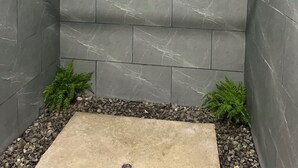 A shower area with grey marble tiles, a small plant, and a pebble border.