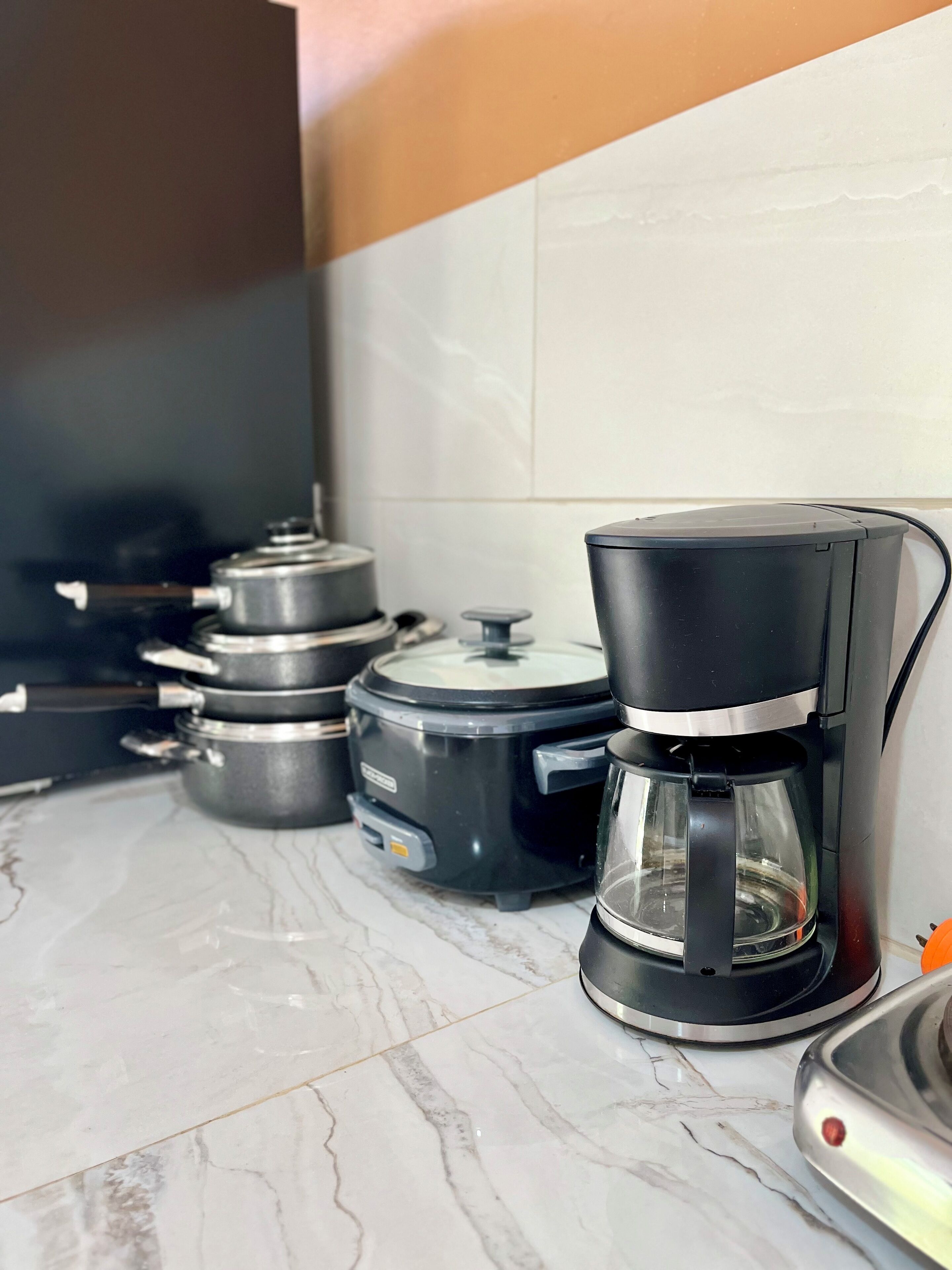 Uma cozinha com cafeteira, panela de cozimento lento e panela de pressão em bancada de mármore.