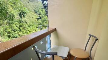 A balcony with a table and two chairs, overlooking a lush green landscape.