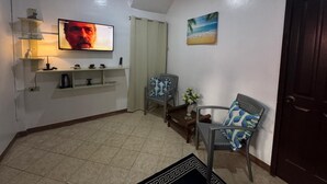 A living room with a television, a painting of a beach, and two wicker chairs. - Ocean Breeze Inn Boracay (Boracay Island)