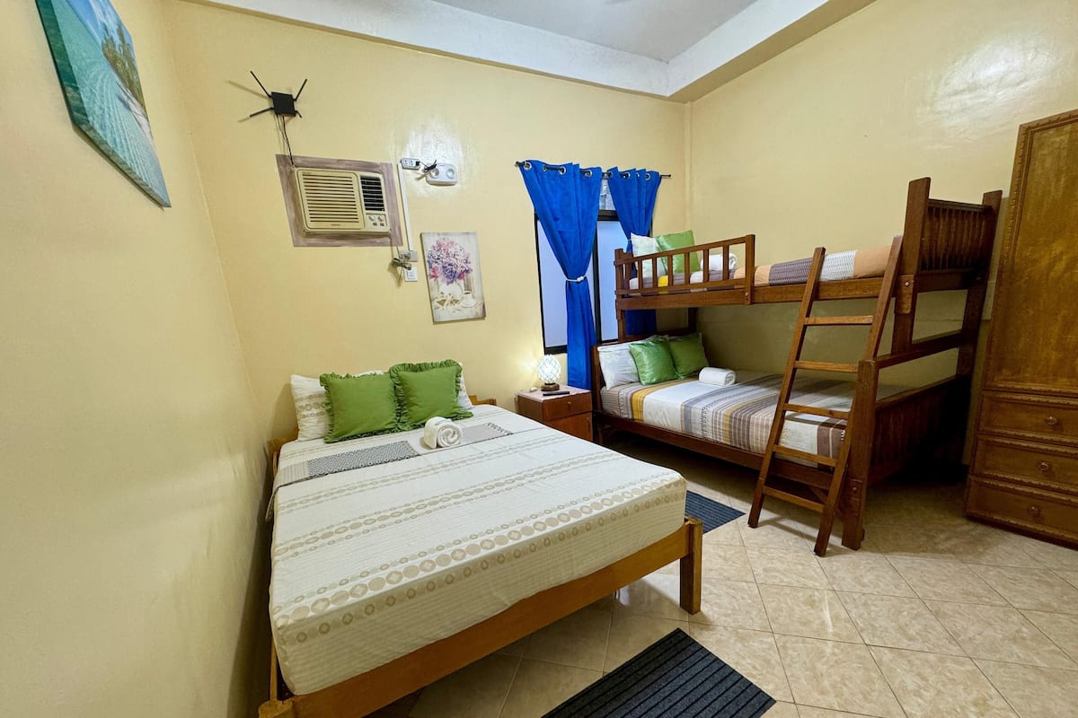 Una habitación con una cama individual, una cama nido, una mesita de noche, una lámpara y un aire acondicionado instalado en la pared.