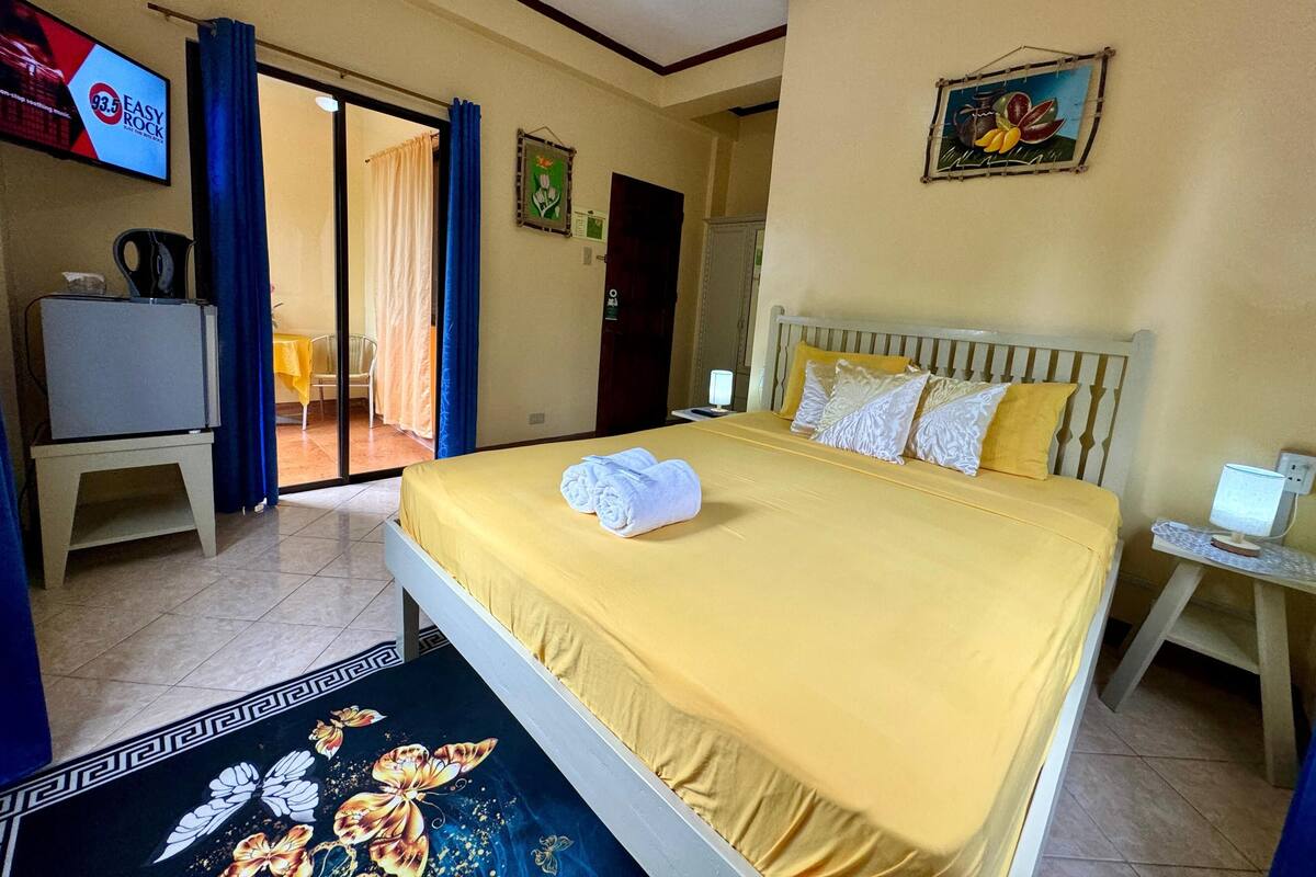 Habitación de hotel con cama, escritorio, televisión y puerta que da a un balcón.