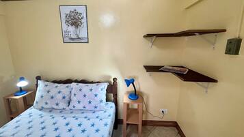 A bedroom with a bed, two bedside lamps, a nightstand, a wall-mounted shelf, and a framed picture.