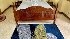 A wooden four-poster bed with a white bedspread and decorative pillows, a wall-mounted air conditioner, and a patterned rug with feather designs. - Ocean Breeze Inn Boracay (Boracay Island)