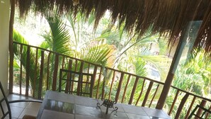 A covered outdoor dining area with a table and chairs, surrounded by a metal railing, and a view of lush greenery. - Beautiful complete 2 bedroom apartment, Tulum Centro! Aluxe (Tulum)