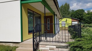 A building with a yellow facade, a red door, and a black metal gate. - Quietly located bungalow with a view of the dam (Zeulenroda-Triebes)