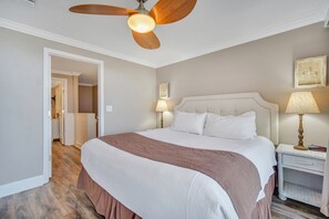 Un dormitorio con una cama grande, un ventilador de techo, dos lámparas de noche y una mesita de noche.
