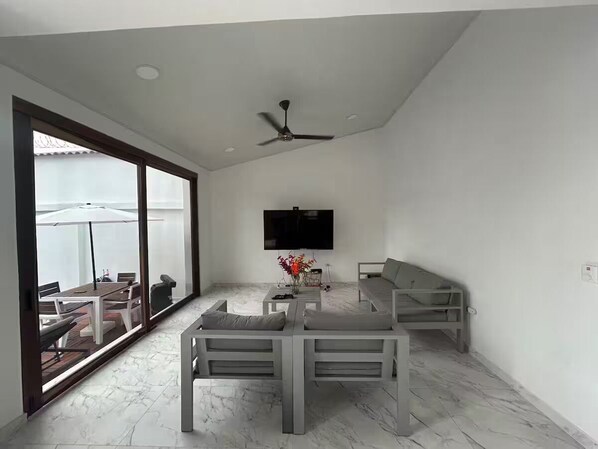 Ein modernes Wohnzimmer mit Flachbildfernseher, Deckenventilator und Essbereich mit Tisch und Stühlen.