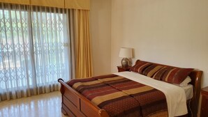 A bedroom with a wooden bed, a nightstand with a lamp, and a window with curtains.