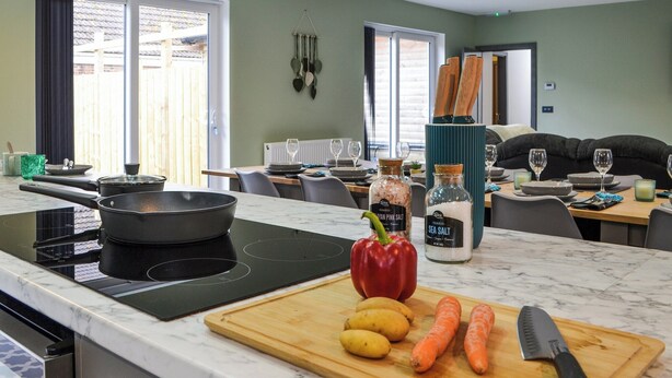Una cocina moderna con una placa de inducción, una tabla de madera con verduras y un cuchillo.