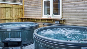 Una cabaña de madera con dos jacuzzis al aire libre, una ventana y una terraza de madera.