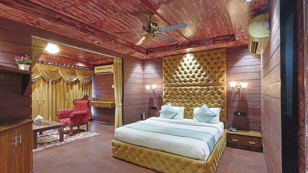 A bedroom with a large bed, a red armchair, a wooden ceiling, and a ceiling fan. - Hotel Venue Inn (Ahmedabad)