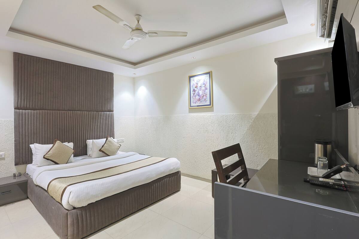 A hotel room with a bed, a desk, a chair, a television, and a ceiling fan.