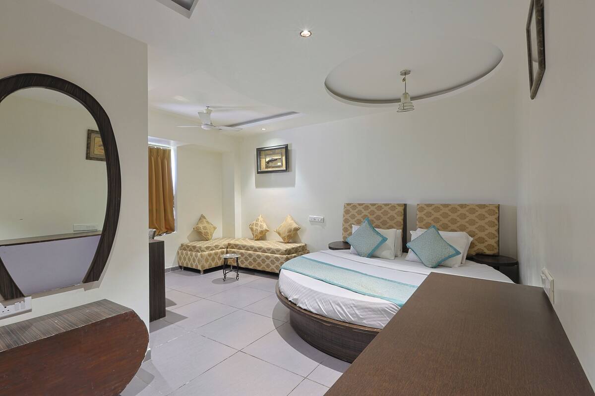 A hotel room with a large bed, a bedside table, a mirror, a ceiling fan, and a small stool.