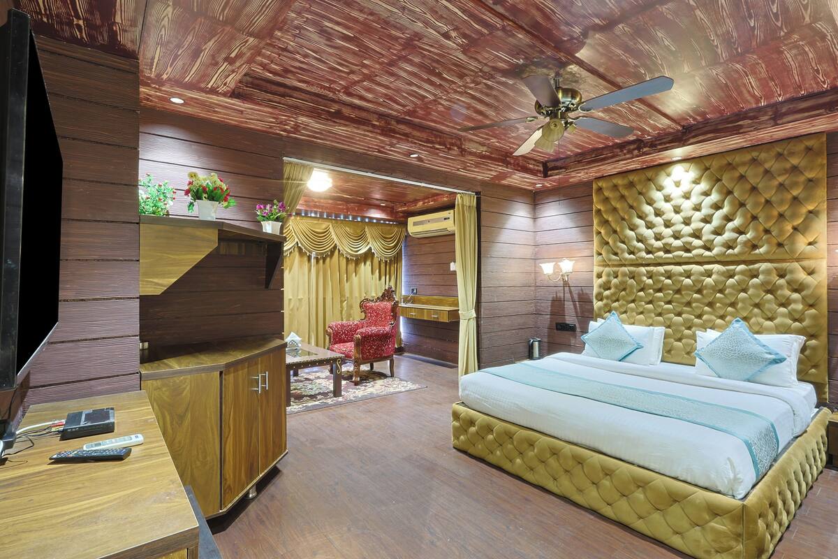 A bedroom with a large bed, a TV, wooden furniture, and a ceiling fan.