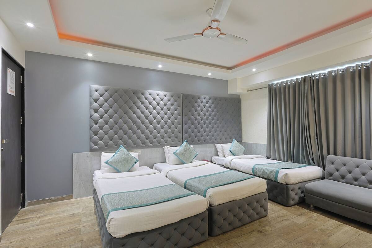 A hotel room with two beds, a grey sofa, and a ceiling fan.