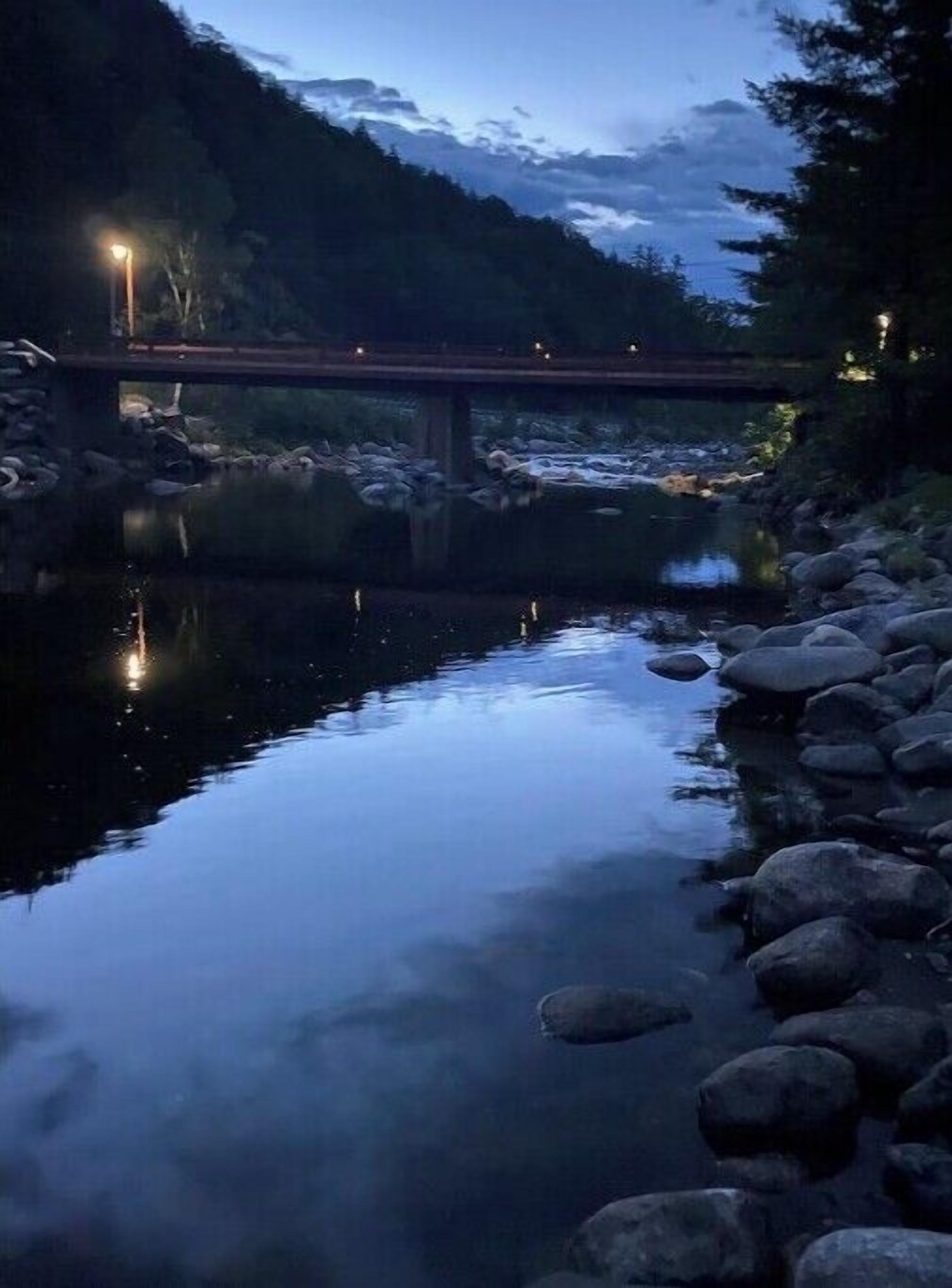 Een rustige rivier met een brug, omringd door rotsen en bomen.