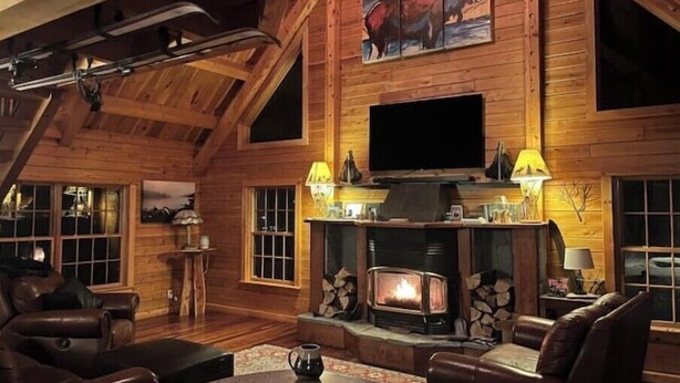 L’intérieur d’un chalet confortable, avec des murs en rondins de bois, une cheminée, des canapés en cuir, un téléviseur et un tableau représentant un élan.