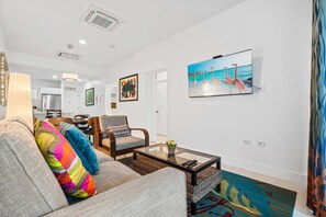 Un salon moderne avec un canapé, des fauteuils, une table basse et un tableau représentant des flamants roses accroché au mur.