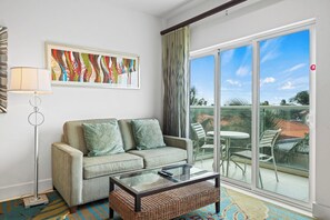 A living room with a sofa, a glass coffee table, a floor lamp, and a view of the outdoors through a sliding glass door. - Resort-Style Amenities! 1BR Condo with Pool Access (Noord)