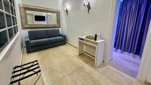 A modern living room with a grey sofa, a white desk, a mirror with an ornate frame, and a blue-lit entrance. - Primus Monti Suites  (Rome)