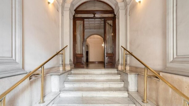 A grand staircase with marble steps and gold handrails, leading to a wooden door framed by a white archway. - Primus Monti Suites  (Rome)