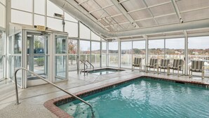 Una piscina interna con pareti in vetro trasparente, una zona coperta con sedie e un segnale di uscita.
