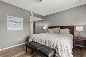 A bedroom with a bed, bench, bedside lamps, and a wall-mounted artwork.