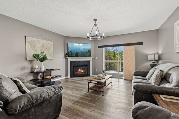 A modern living room with leather sofas, a fireplace, a television, and a large window with a view.