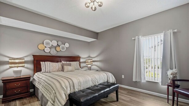 Una camera da letto con un letto grande, un comodino in legno, una panca, un lampadario a soffitto e una finestra con tende.