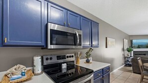 Una cucina moderna con mobili blu, un forno a microonde in acciaio inossidabile, un forno e un'area pranzo con tavolo e sedie.