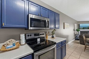 A modern kitchen with blue cabinets, a stainless steel microwave, an oven, and a dining area with a table and chairs. - 3 BR/3 BA Recently Updated Pigeon Forge Condo - Walk to Pkwy - Free Tickets (Pigeon Forge)