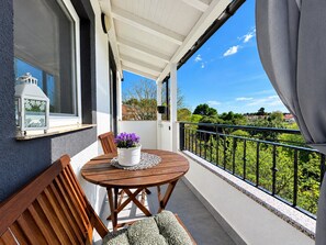 Un balcon avec une table en bois, des chaises et un pot de fleurs.