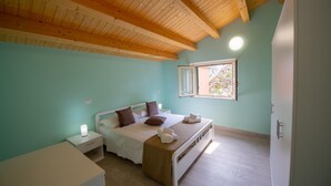 A bedroom with a wooden ceiling, a bed with pillows, a bedside table with a lamp, and a window with a view of trees. - Seaside Residence with Aeolian Islands View – Pool, Gym & WiFi – Apt PANAREA (Patti)