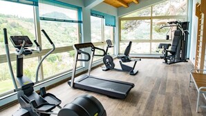 A gym with cardio machines, weight equipment, and large windows offering a view of greenery. - Seaside Residence with Aeolian Islands View – Pool, Gym & WiFi – Apt PANAREA (Patti)