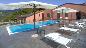 A rooftop pool with white lounge chairs and umbrellas, surrounded by a building with a red facade and green shutters. - Seaside Residence with Aeolian Islands View – Pool, Gym & WiFi – Apt PANAREA (Patti)