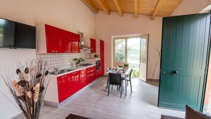 A modern kitchen with red cabinets, a dining area with a table and chairs, and a green door. - Seaside Residence with Aeolian Islands View – Pool, Gym & WiFi – Apt PANAREA (Patti)