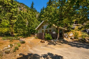 Une cabane dotée d’une terrasse en bois, entourée d’une forêt dense et d’un terrain rocheux.