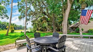 Une terrasse dotée d’une table ronde et de chaises, entourée d’arbres et offrant une vue sur un terrain de golf.
