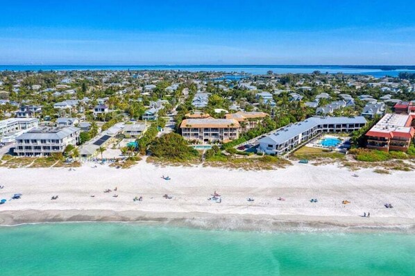 Vista aérea de una zona turística costera con propiedades frente a la playa, una playa de arena y aguas azules cristalinas.